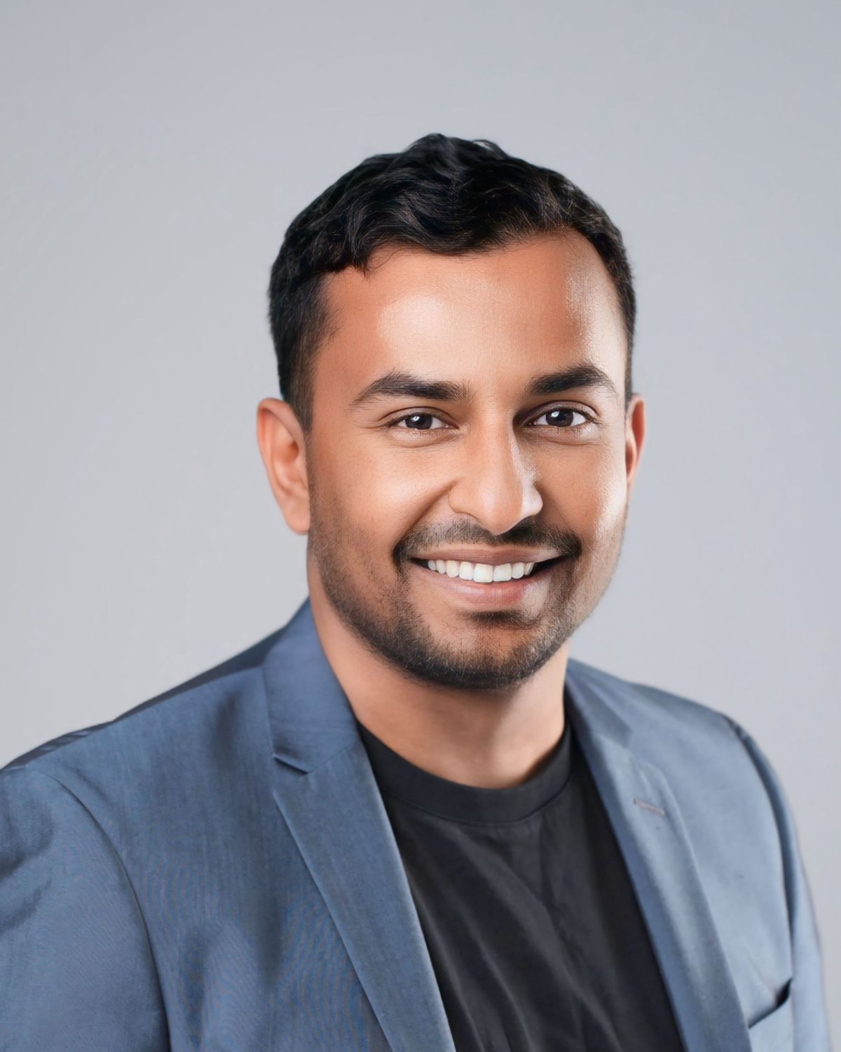 Dinuka Gunaratne smiling, wearing a blue blazer over a black T-shirt